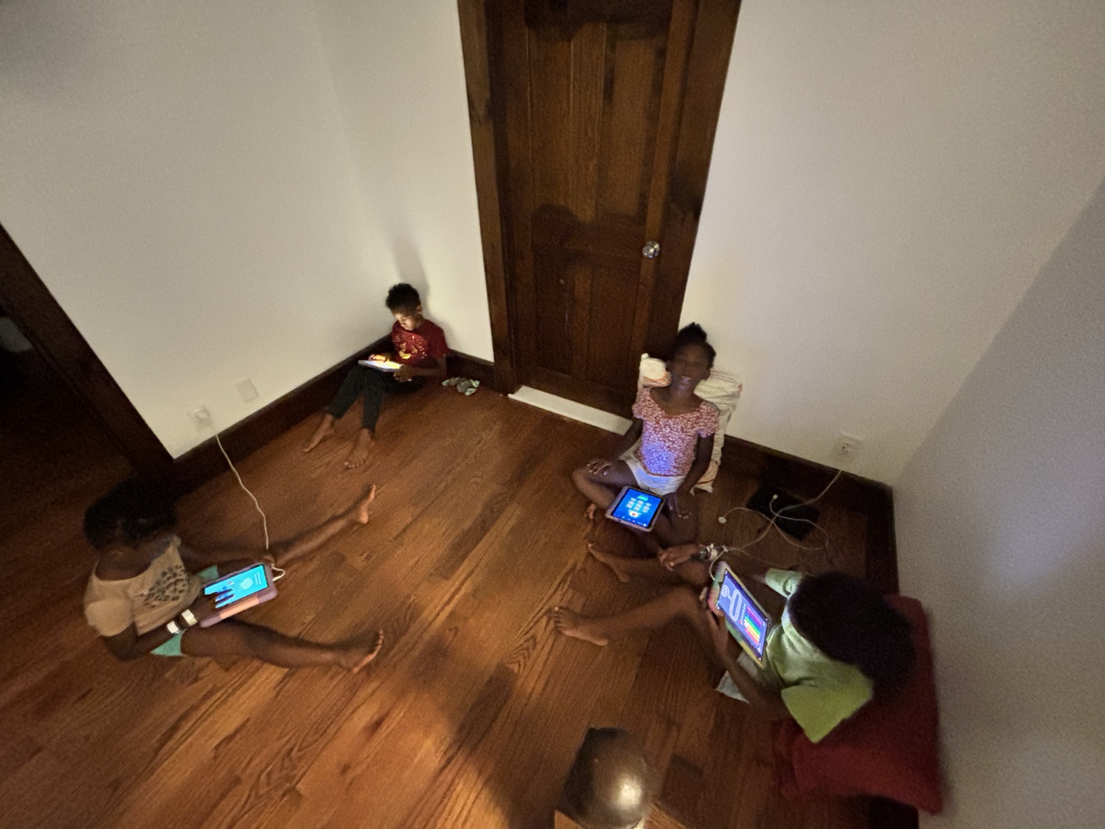 Four kids sitting on the floor of a dim room, each lit by a tablet