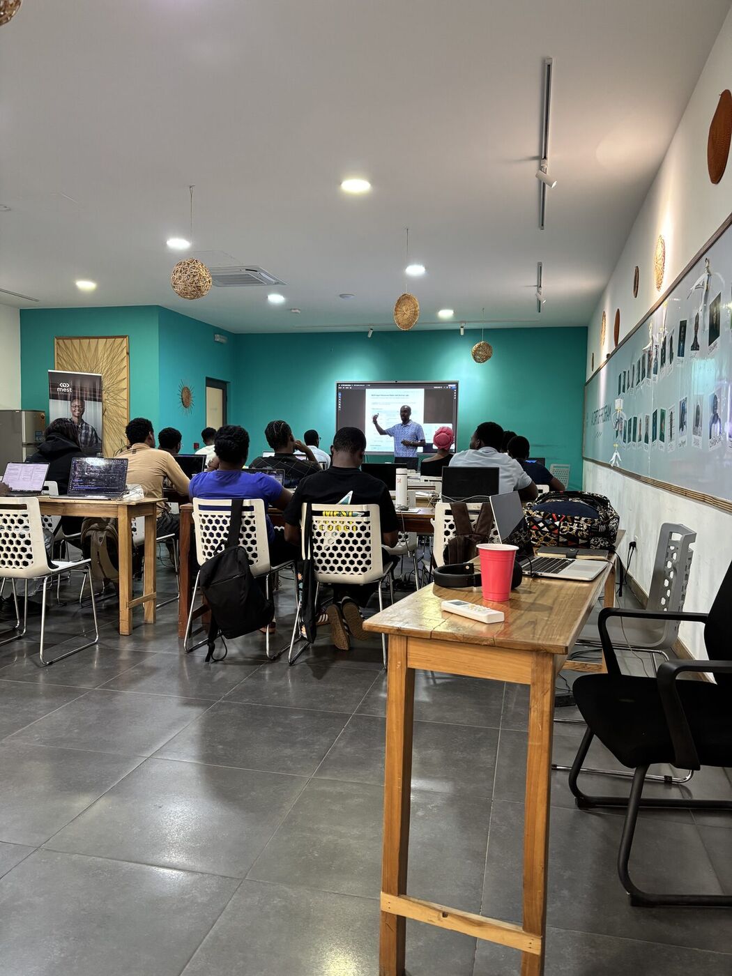 The MEST classroom seen from the back: rows of founders at laptops facing a screen where Waziri is teaching.